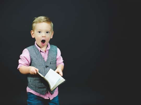 A photo of an astonished kid with a book, knowing about Islam.